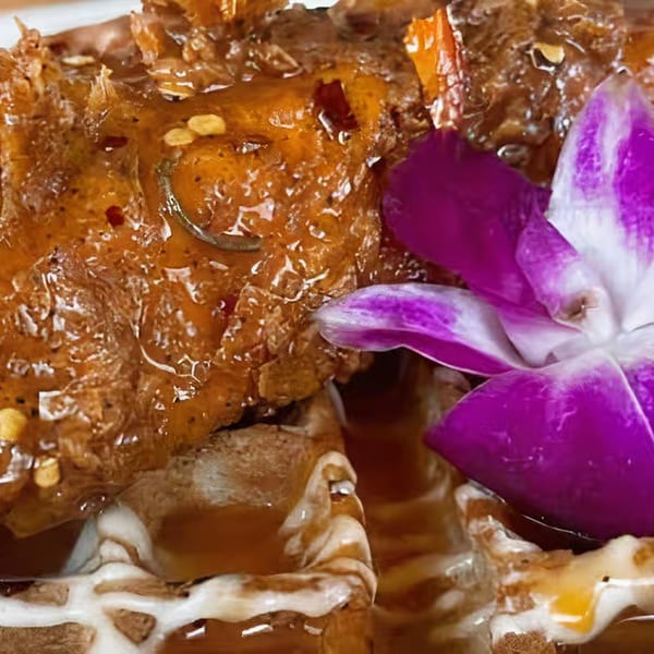 Close-up of Soul Vibez's chicken and waffles, drizzled with sauce and garnished with a purple orchid.