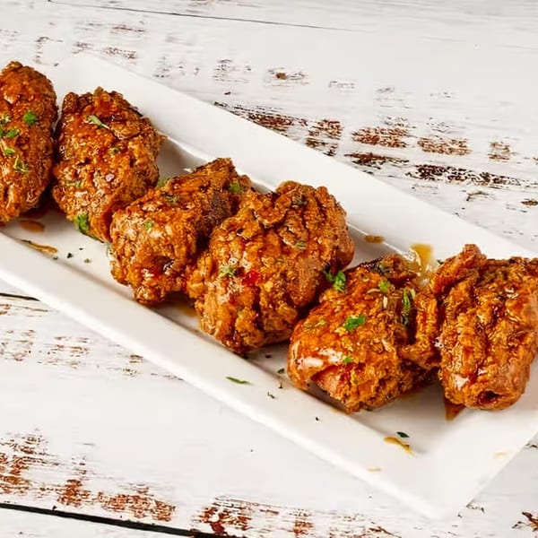 Six crispy, glazed Soul Vibez chicken wings garnished with herbs on a white rectangular plate.